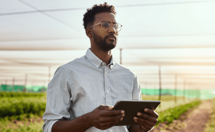 A professional agricultural economist standing in a greenhouse holding a digital tablet, looking focused and ready to apply economic principles to agribusiness.